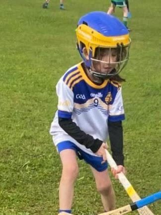A young camogie player in a helmet crouching low over her hurl