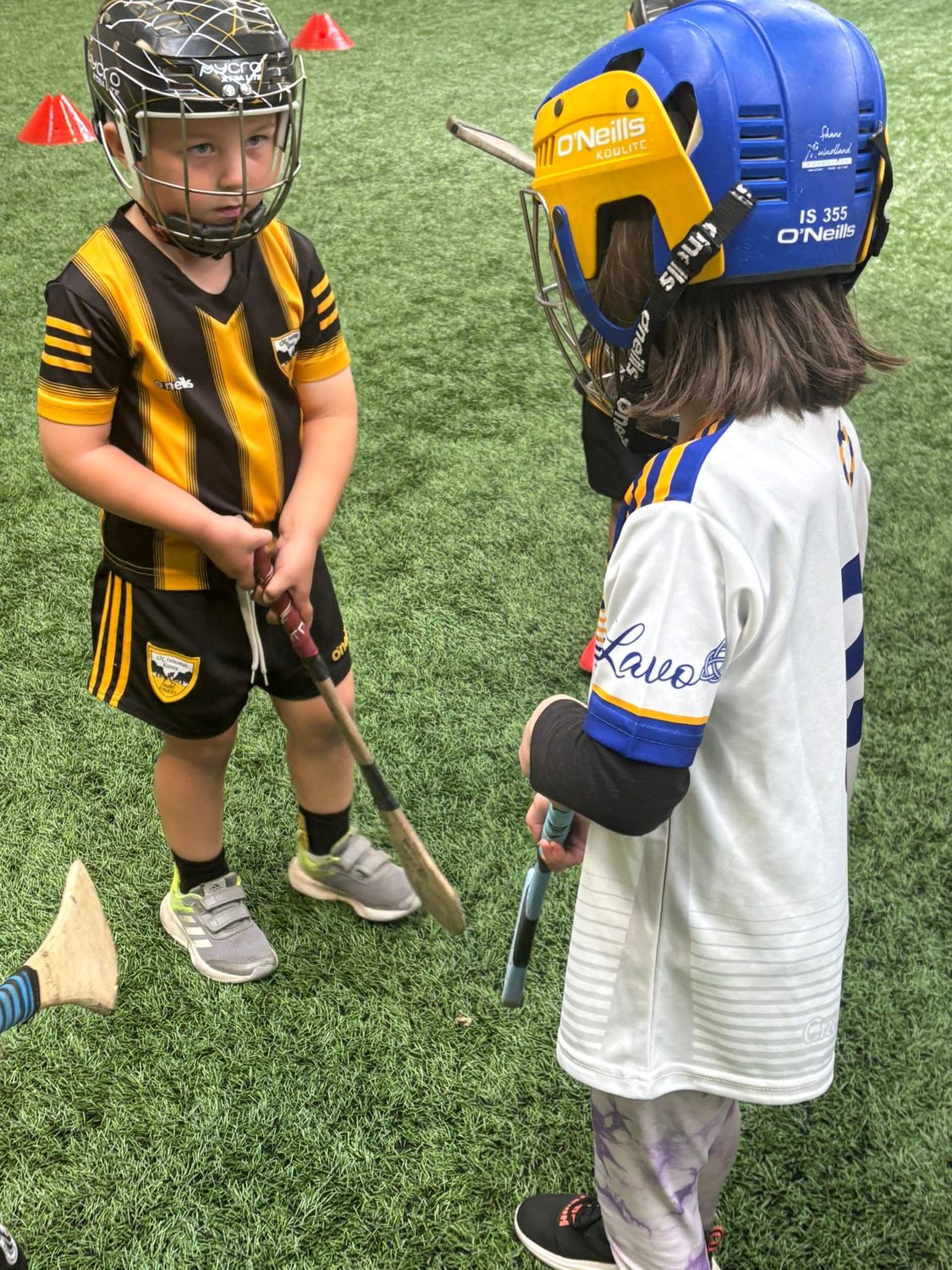 Two children in helmets working on their first touch with hurls on the 3G surface