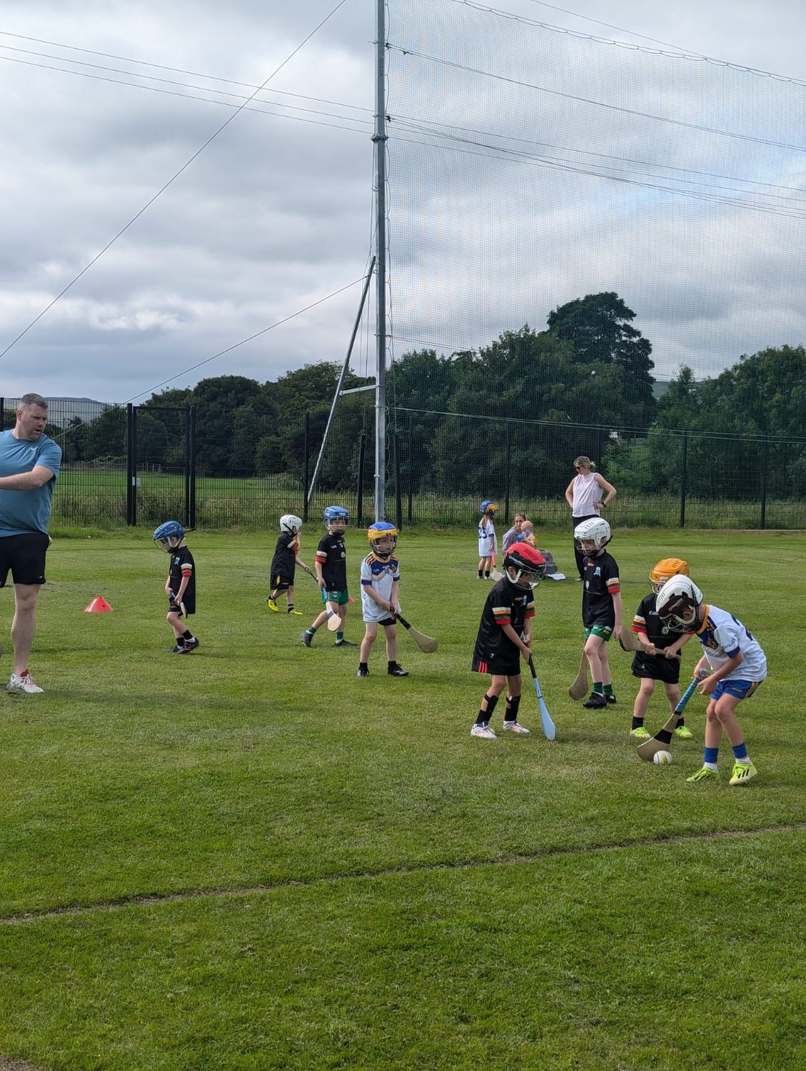 A large group of children with hurls and helmets spread out across the pitch at a training session